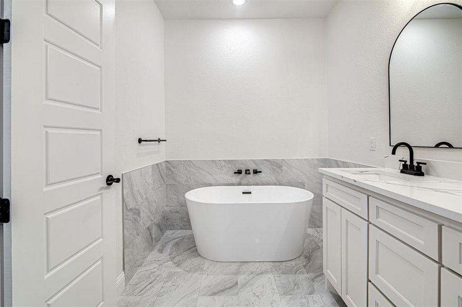 Bathroom featuring vanity, a bath, and tile walls