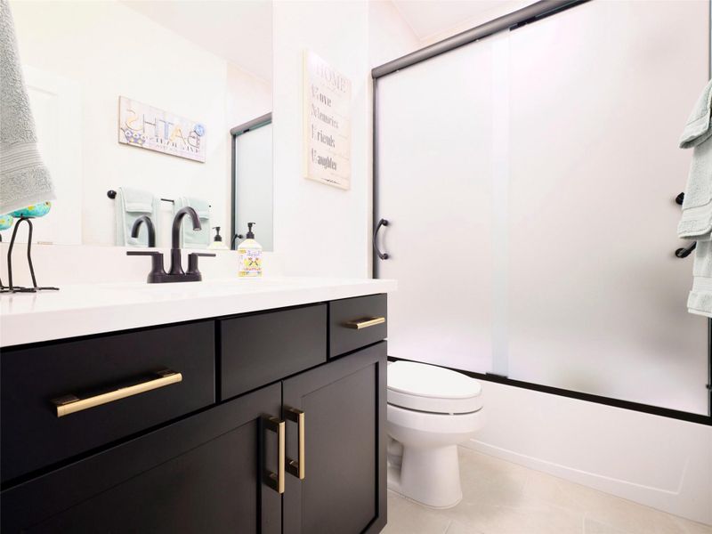 Modern bathroom with a sleek black vanity, gold hardware, and a white countertop. Features a frosted glass shower door for added elegance.