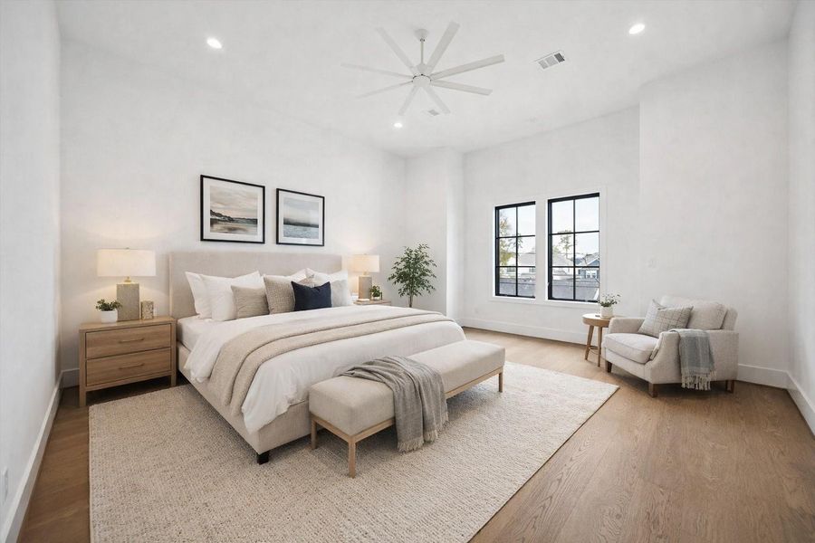 Spacious primary suite with vaulted ceilings, wide plank hardwood floors, and expansive black framed windows for abundant natural light. Crisp white walls, recessed lighting, and a modern ceiling fan enhance the airy, open layout, creating a serene retreat designed for comfort and relaxation. *Virtually Staged*