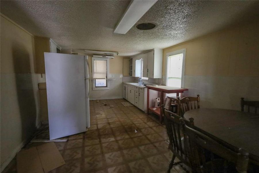 Kitchen with freestanding refrigerator, white cabinets, light countertops, dark flooring, and a textured ceiling Kitchen with freestanding refrigerator, white cabinets, light countertops, dark flooring, and a textured ceiling