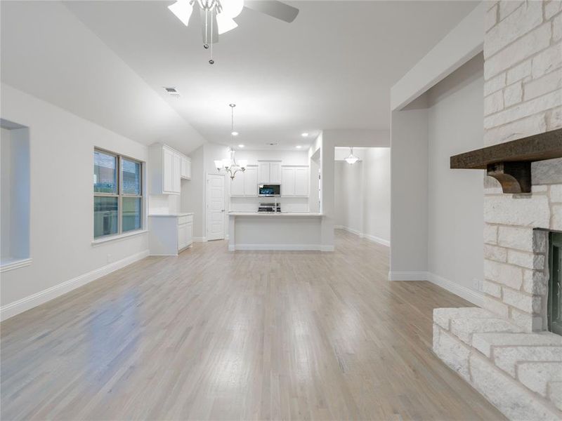 Unfurnished living room with a fireplace, light wood-type flooring, ceiling fan with notable chandelier, and vaulted ceiling