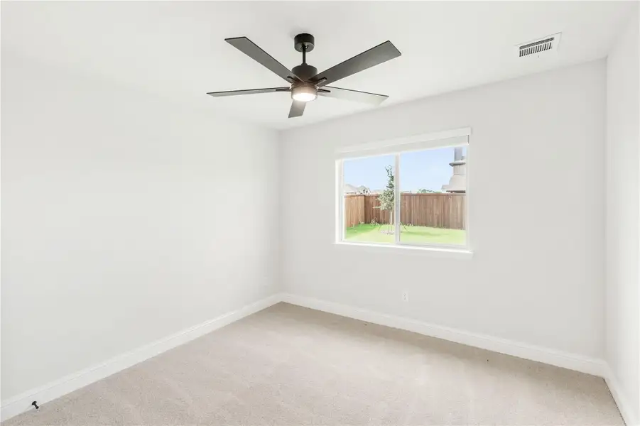 Empty bedroom with carpet flooring, ceiling fan, and window overlooking fenced backyard