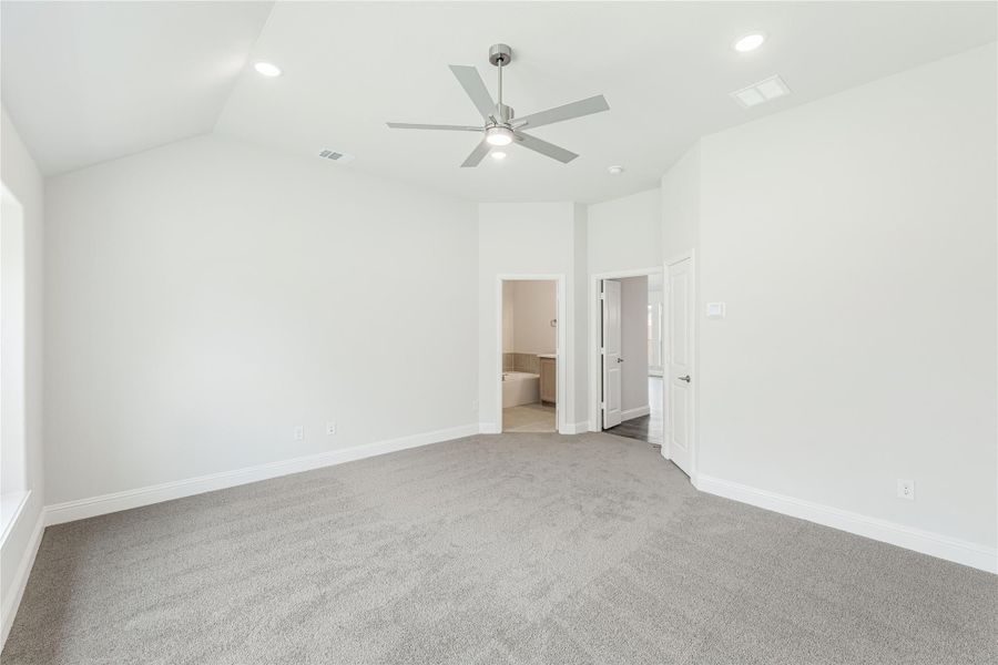 Empty bedroom with vaulted ceiling, ceiling fan, gray carpet, and ensuite bathroom doorway Empty bedroom with vaulted ceiling, ceiling fan, gray carpet, and ensuite bathroom doorway