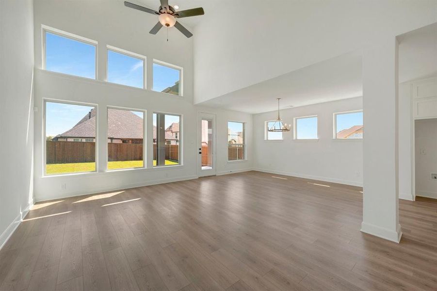 Spacious room featuring high ceilings, wood-finish flooring, a contemporary ceiling fan, and multiple windows providing natural illumination