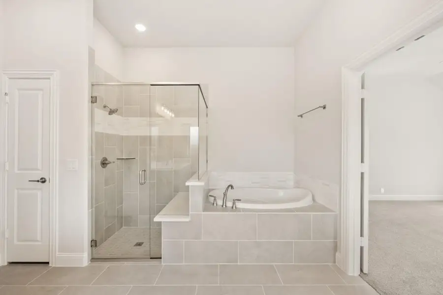 Master bathroom with glass-enclosed tile shower and raised soaking tub on tiled platform