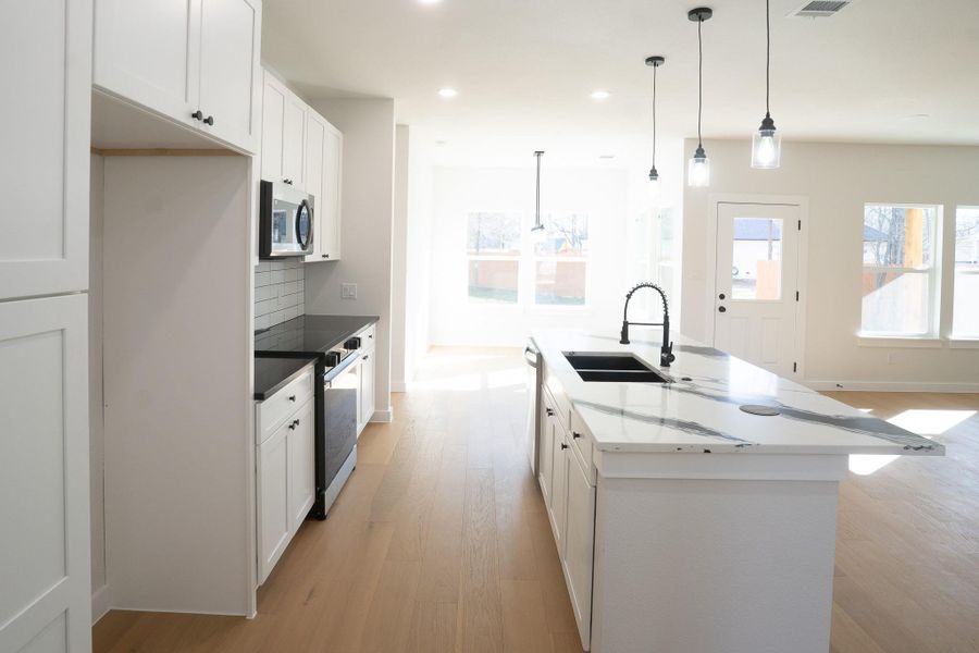 Kitchen with white cabinetry, appliances with stainless steel finishes, decorative backsplash, decorative light fixtures, and light wood-type flooring