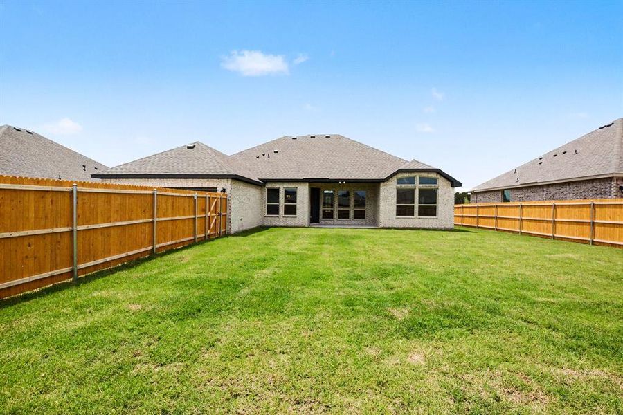 Expansive backyard featuring a manicured lawn, full privacy fencing, light-colored brick exterior, a large bay window, and a patio door Expansive backyard featuring a manicured lawn, full privacy fencing, light-colored brick exterior, a large bay window, and a patio door