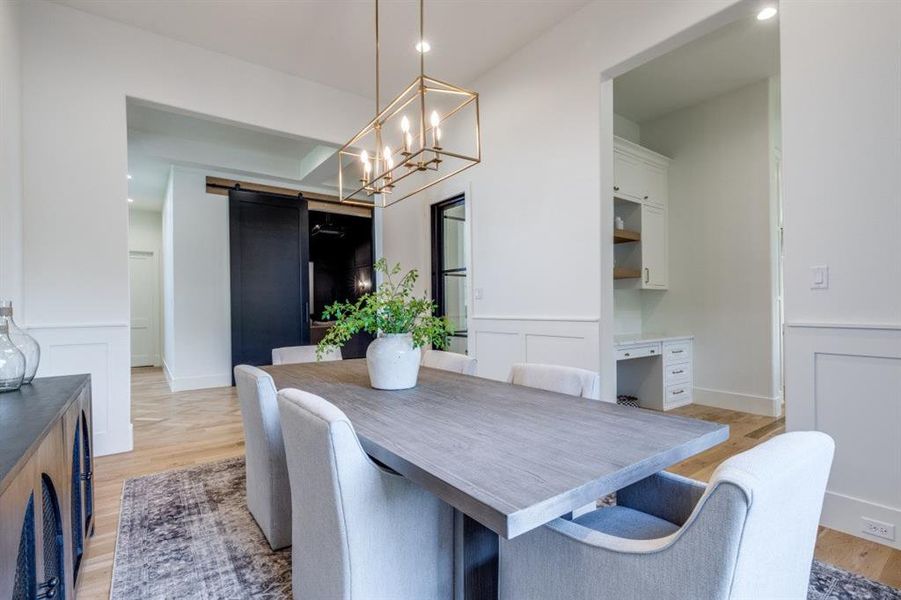 Dining area featuring a barn door, a decorative wall, a wainscoted wall, light wood-type flooring, and a chandelier Dining area featuring a barn door, a decorative wall, a wainscoted wall, light wood-type flooring, and a chandelier