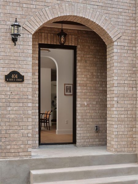 An inviting brick arched entryway with classic sconce and pendant lighting frames the welcoming front door.