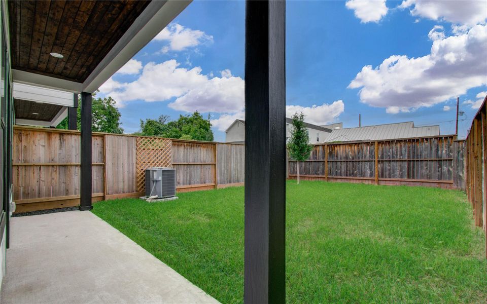 This photo showcases a backyard with a covered patio area, a neatly maintained lawn, and a wooden privacy fence, providing a cozy and private outdoor space.