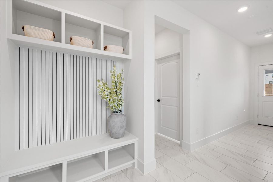 Welcoming foyer with built-in bench seating and storage cubbies. The space features sleek tile flooring, recessed lighting, and a view into an first floor room with stylish decor.