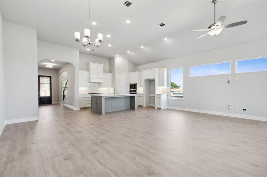 Unfurnished living room featuring ceiling fan with notable chandelier, light hardwood / wood-style flooring, and lofted ceiling