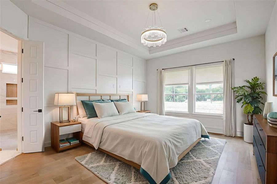Bedroom with a tray ceiling, light wood-style floors, and a chandelier