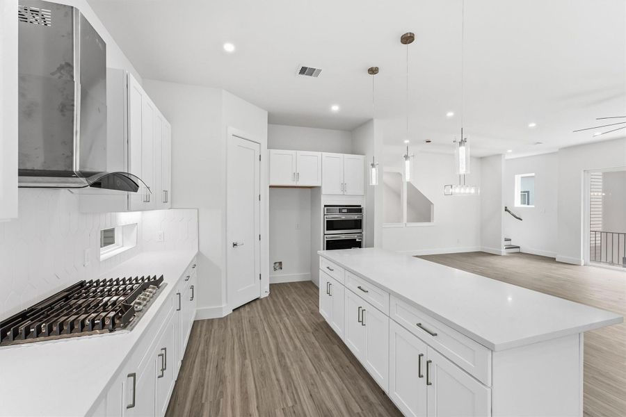Another view highlighting the expansive island, gas cooktop, vent hood, wall oven, and ample cabinetry.