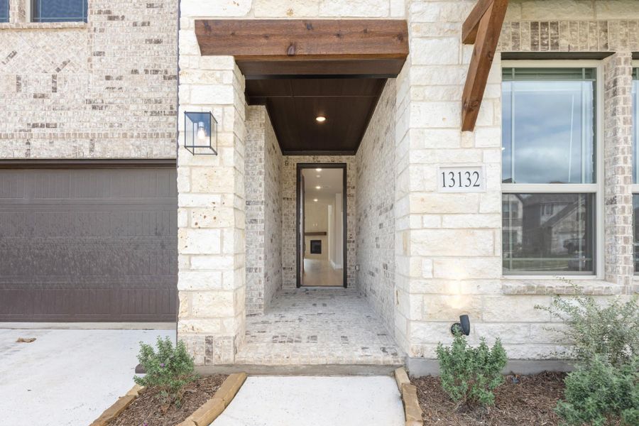 Home entrance with limestone exterior, wood beam overhang, and glass front door at address 13132