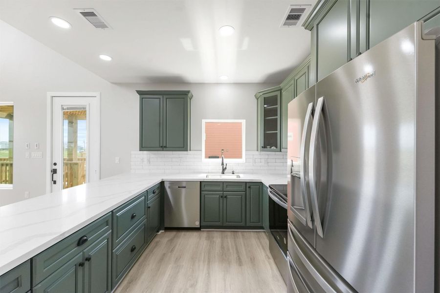 This kitchen features modern green cabinetry, stainless steel appliances, and a bright, open layout. It includes a large countertop, subway tile backsplash, and recessed lighting, creating a stylish and functional space. This kitchen features modern green cabinetry, stainless steel appliances, and a bright, open layout. It includes a large countertop, subway tile backsplash, and recessed lighting, creating a stylish and functional space.