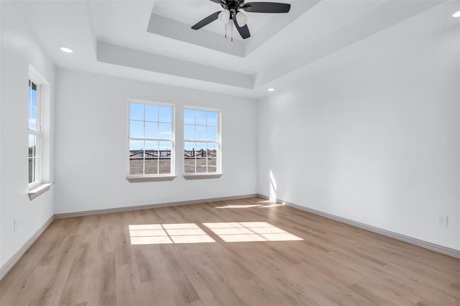 Unfurnished room with light hardwood / wood-style floors, ceiling fan, and a tray ceiling