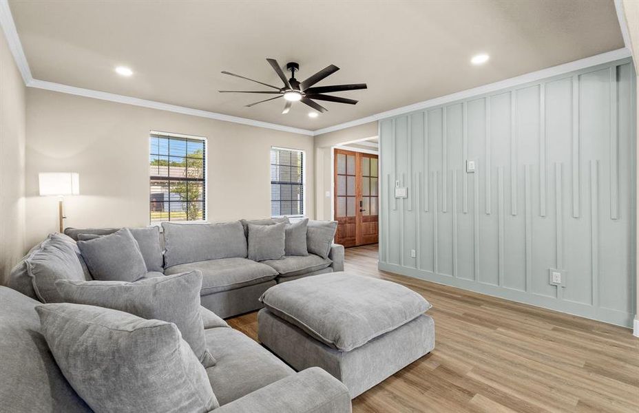 Spacious living area featuring light wood-finish flooring, a contemporary ceiling fan, recessed lighting, and a decorative accent wall with vertical paneling