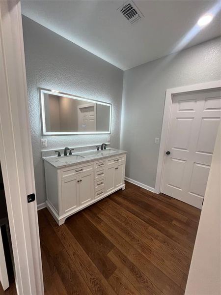 Bathroom featuring a textured wall, double vanity, and dark wood finished floors Bathroom featuring a textured wall, double vanity, and dark wood finished floors