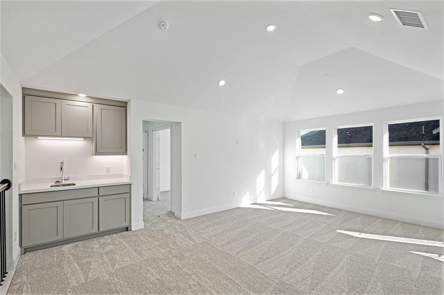 Unfurnished living room with vaulted ceiling, sink, and light colored carpet