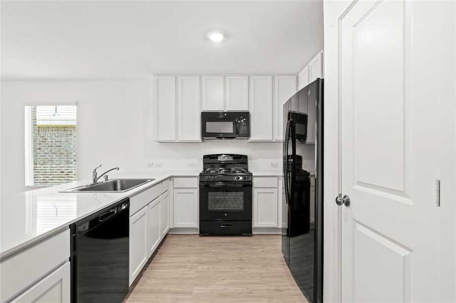 Kitchen featuring white cabinetry, black appliances, a double basin sink, light-toned wood-finish flooring, and white countertops