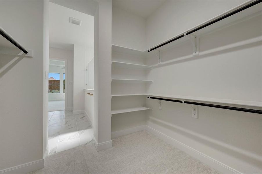 Spacious walk-in closet featuring extensive built-in shelving, dual hanging rods, light-toned carpeting, and crisp white walls Spacious walk-in closet featuring extensive built-in shelving, dual hanging rods, light-toned carpeting, and crisp white walls