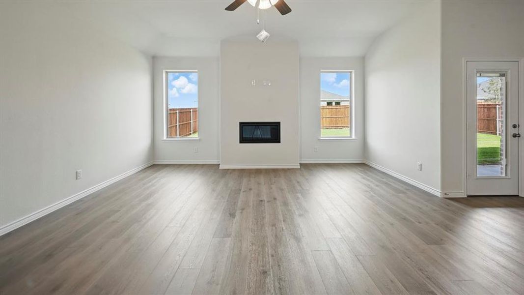 Unfurnished living room featuring light wood finished floors, plenty of natural light, a ceiling fan, and a glass covered fireplace