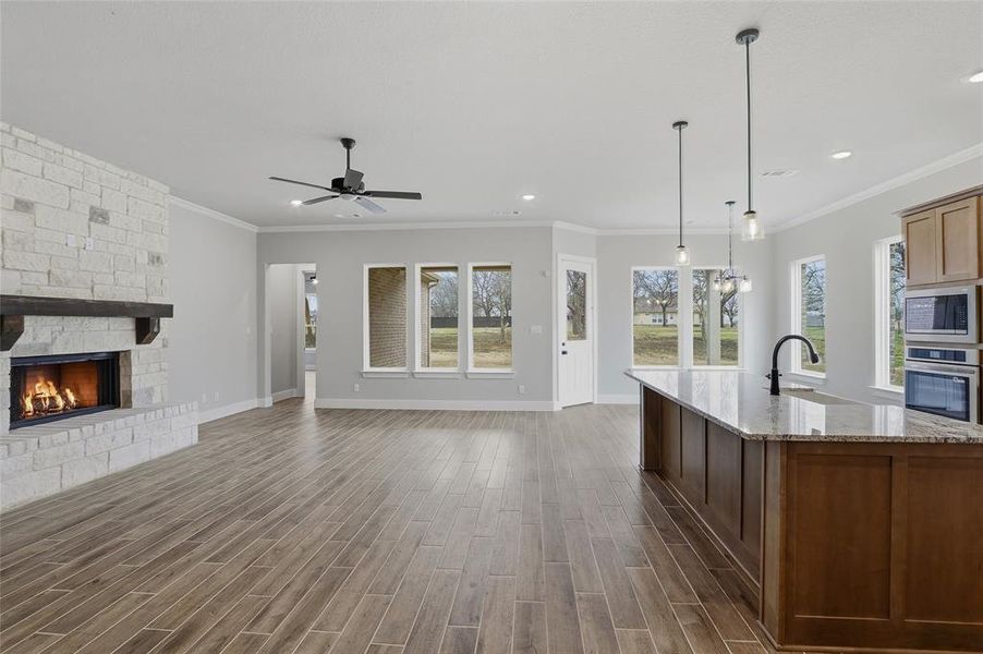 Kitchen with a stone fireplace, wood tiled floors, open floor plan, a center island with sink, and crown molding