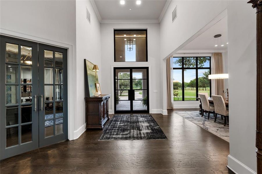 Foyer entrance with crown molding, a towering ceiling, dark wood-type flooring, and french doors