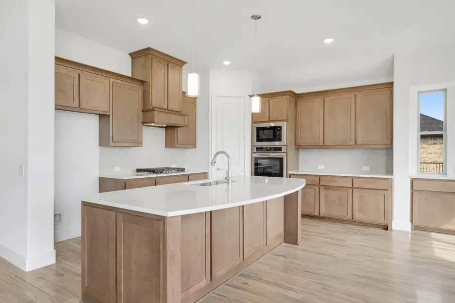 Kitchen with large center island, wood cabinets, white countertops, and stainless steel appliances on light hardwood floors Kitchen with large center island, wood cabinets, white countertops, and stainless steel appliances on light hardwood floors