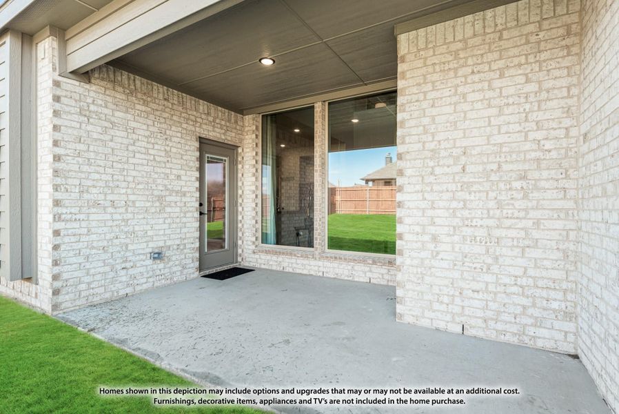 Covered back patio with concrete floor, white brick exterior, glass door, and large window overlooking fenced yard.