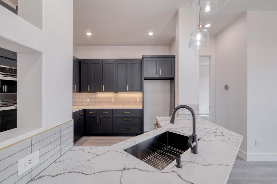 Kitchen with multiple ovens, pendant lighting, light stone counters, a sink, and decorative backsplash