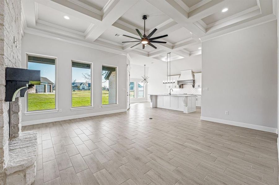 Unfurnished living room featuring ceiling fan, a stone fireplace, beam ceiling, light wood-style floors, and coffered ceiling