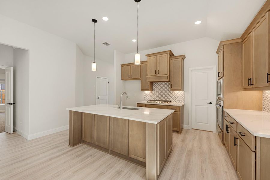 Kitchen with large center island, light wood cabinets, quartz countertops, and pendant lights over sink