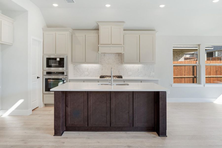 Kitchen with dark wood island, white cabinets, marble backsplash, and stainless steel double ovens