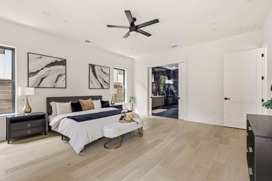 Spacious bedroom featuring light wood-finish flooring, a modern black ceiling fan, and recessed lighting