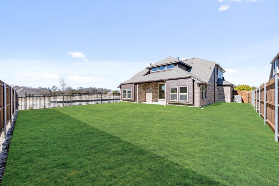 Backyard of brick home with large green lawn, wood and iron fencing, and covered patio area. Backyard of brick home with large green lawn, wood and iron fencing, and covered patio area.