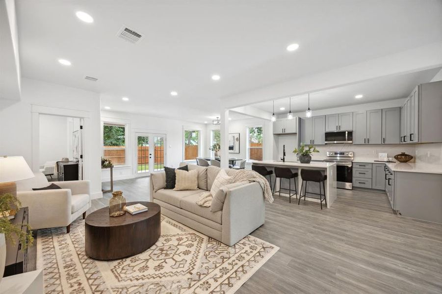 Living room with wood-style floors, open to the kitchen, dining area and back patio