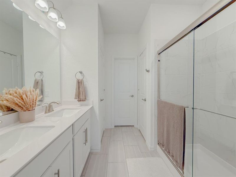 Bathroom with double vanity, a shower stall, baseboards, and a sink