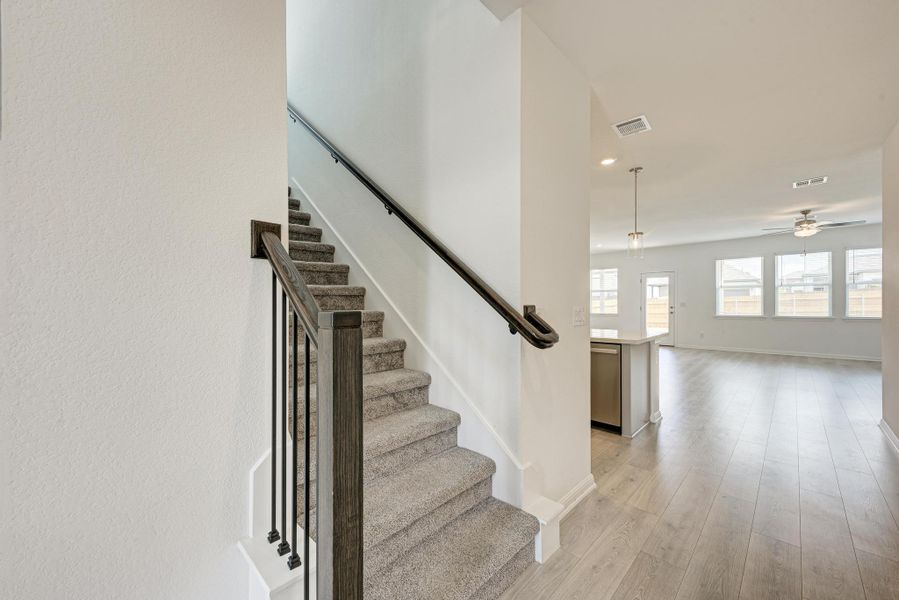 A welcoming entry featuring a carpeted staircase with wood and iron railings, leading to an open-concept living space with light-toned flooring.