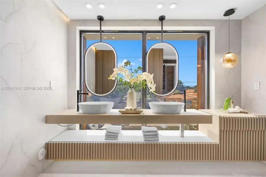 Floating vanity featuring dual vessel sinks, matte black wall-mounted faucets, oval-shaped hanging mirrors, and fluted wood-finish cabinetry with built-in storage Floating vanity featuring dual vessel sinks, matte black wall-mounted faucets, oval-shaped hanging mirrors, and fluted wood-finish cabinetry with built-in storage