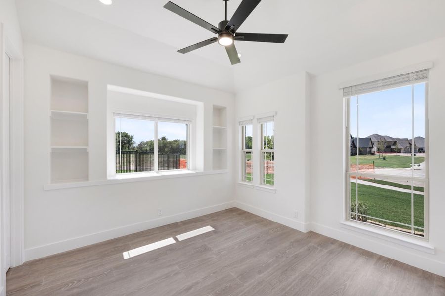 Empty room with white walls, built-in shelves, ceiling fan, and wood-look floors with large windows