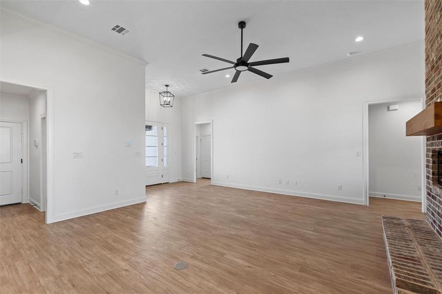 Unfurnished living room with light wood-type flooring, a ceiling fan, a brick fireplace, crown molding, and recessed lighting Unfurnished living room with light wood-type flooring, a ceiling fan, a brick fireplace, crown molding, and recessed lighting