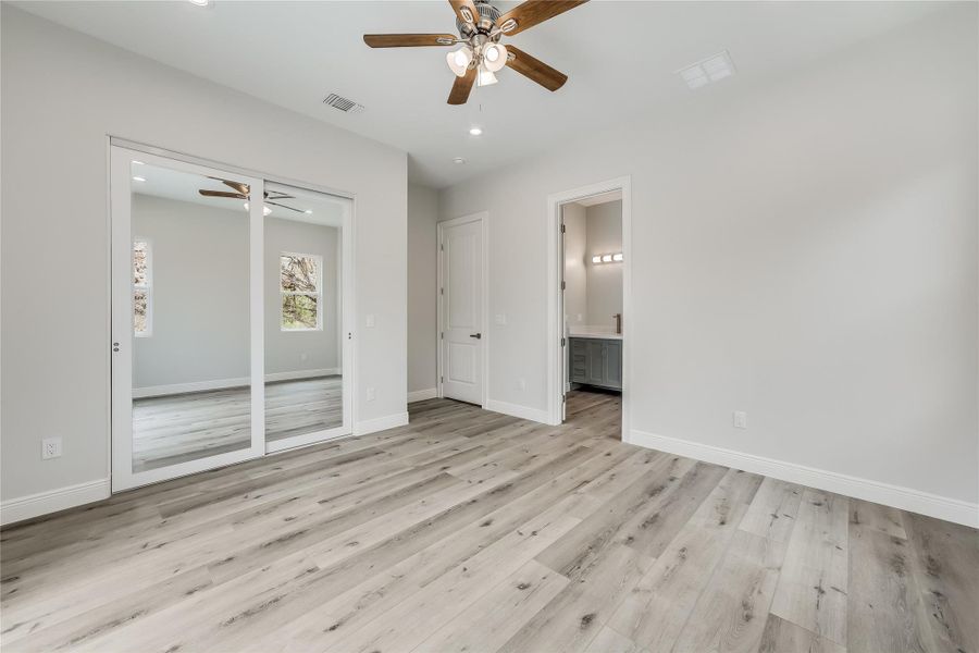 Unfurnished bedroom featuring ceiling fan, ensuite bathroom, and light wood-type flooring