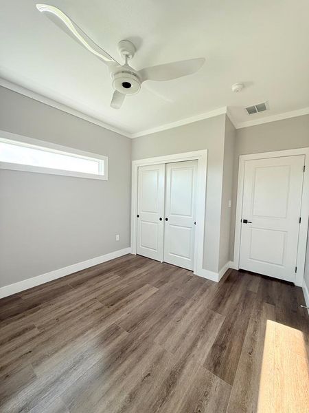 A well-lit bedroom features durable laminate flooring and a modern ceiling fan.