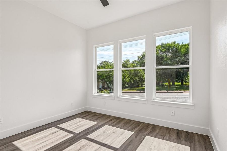 Spacious room featuring three large windows, wood-finish flooring, white baseboards, and a ceiling fan