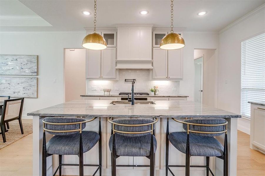 Kitchen featuring white cabinetry, an island with sink, decorative backsplash, and light wood-type flooring