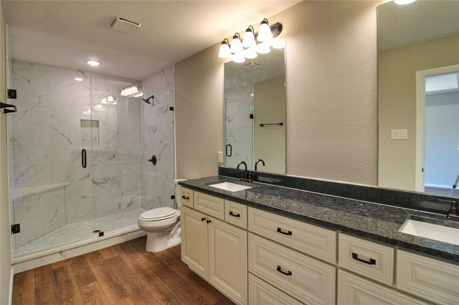 Bathroom featuring dark wood-style flooring, a marble finish shower, and double vanity