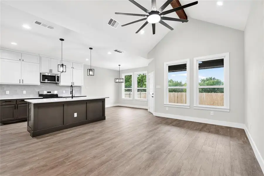 Spacious interior room featuring vaulted ceilings, a prominent exposed wood beam, and a modern ceiling fan with multiple blades