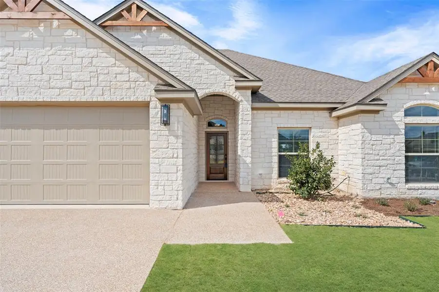 View of front of property featuring stone siding, an attached garage, a front yard, concrete driveway, and roof with shingles